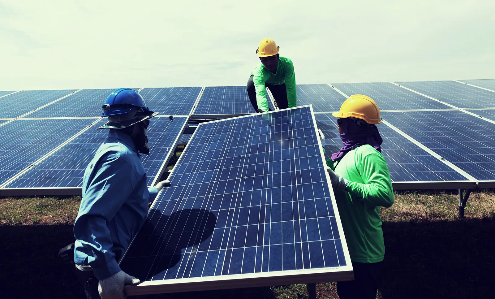  In Jaipur, Rajasthan, three men wearing hard hats and safety vests collaborate on the installation of a solar panel.